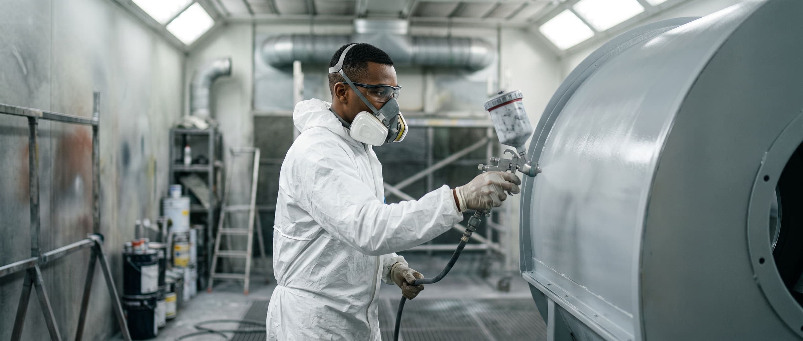 Peintre industriel appliquant une peinture au pistolet sur un carter de machine dans une cabine de peinture